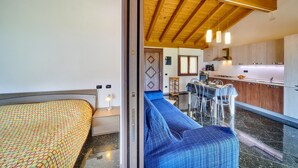 A modern interior with a wooden ceiling, a dining area with bar stools, a kitchen with wooden cabinets, and a bed with a patterned bedspread. - APARTMENT 1 BEDROOM WITH A FANTASTIC VIEW OF LAKE COMO (Gravedona Ed Uniti)