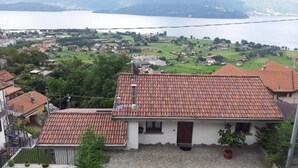 A residential area with houses featuring red-tiled roofs, a cobblestone courtyard, and a view of a lake with mountains in the background. - APARTMENT 1 BEDROOM WITH A FANTASTIC VIEW OF LAKE COMO (Gravedona Ed Uniti)