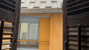 A view through a wooden gate into a building with a tiled roof, a window, and a yellow wall. - Cozy and small apartment in the heart of vauban - briancon (Briançon)