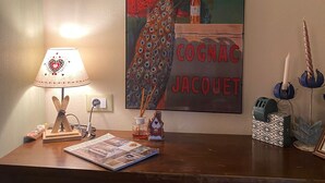 A wooden desk with a lamp, a framed poster, and various decorative items. - Cozy and small apartment in the heart of vauban - briancon (Briançon)