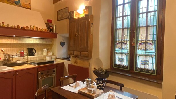 A cozy kitchen with wooden beams, a dining table with chairs, a stove, and a window with stained glass. - Cozy and small apartment in the heart of vauban - briancon (Briançon)