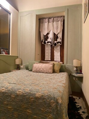 Une chambre à coucher avec un grand lit, deux tables de chevet avec des lampes, une fenêtre avec des rideaux et un miroir au mur.
