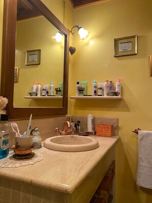 Une salle de bain équipée d’un lavabo, d’un miroir et d’étagères où sont rangés les articles de toilette.