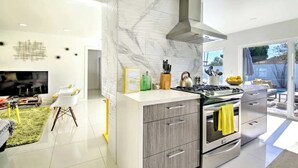 A modern kitchen with a marble backsplash, stainless steel appliances, and a large island with a yellow towel. - Amarillo House - Luxury Home With Pool Spa (Palm Springs)