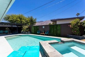 Piscina con escalones y sillas, rodeada de un jardín ajardinado y vistas a la montaña.