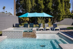 Una piscina con ombrellone blu, sedie a sdraio e una bordura piastrellata decorata.