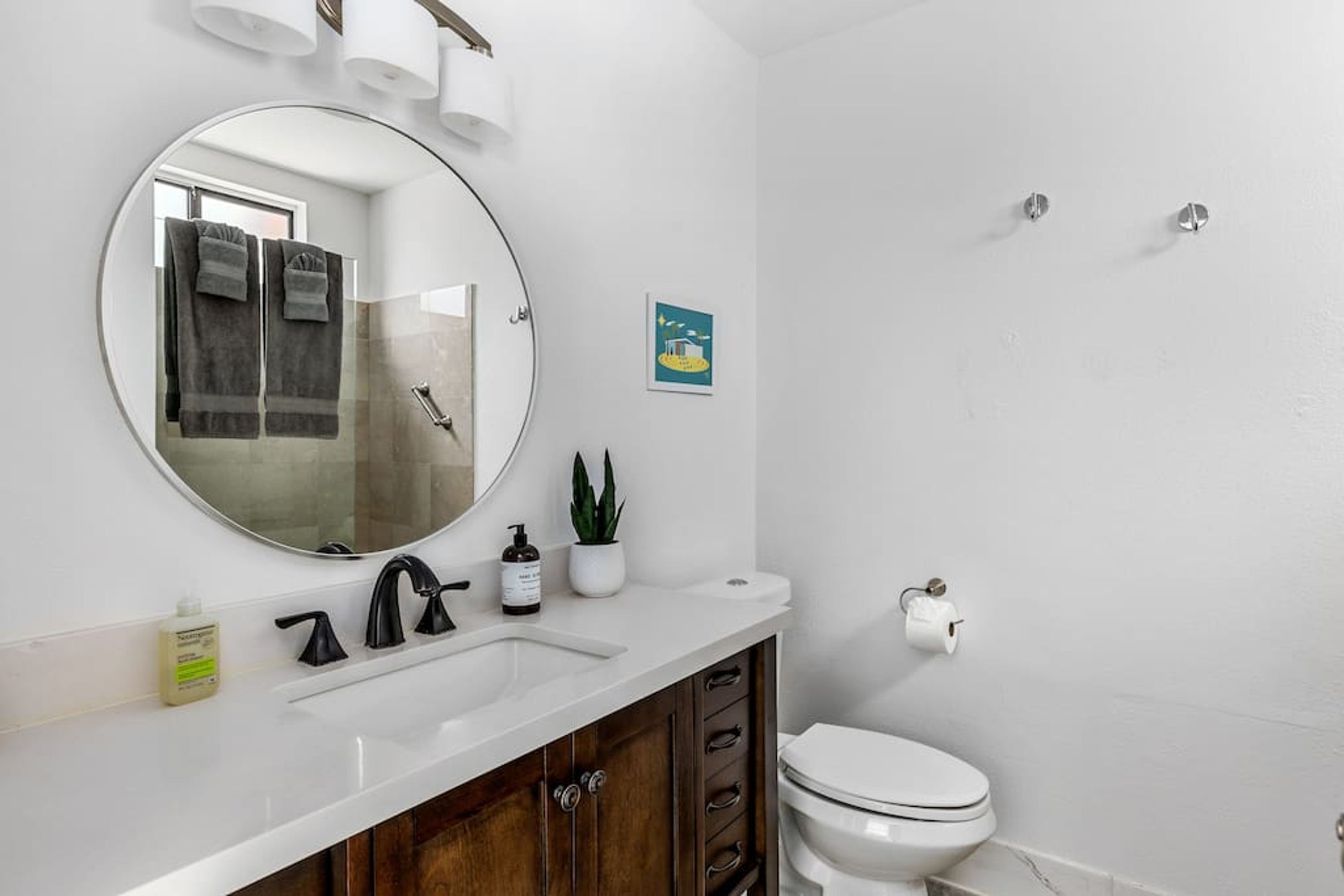 A bathroom with a round mirror, a sink, a toilet, and a small potted plant.
