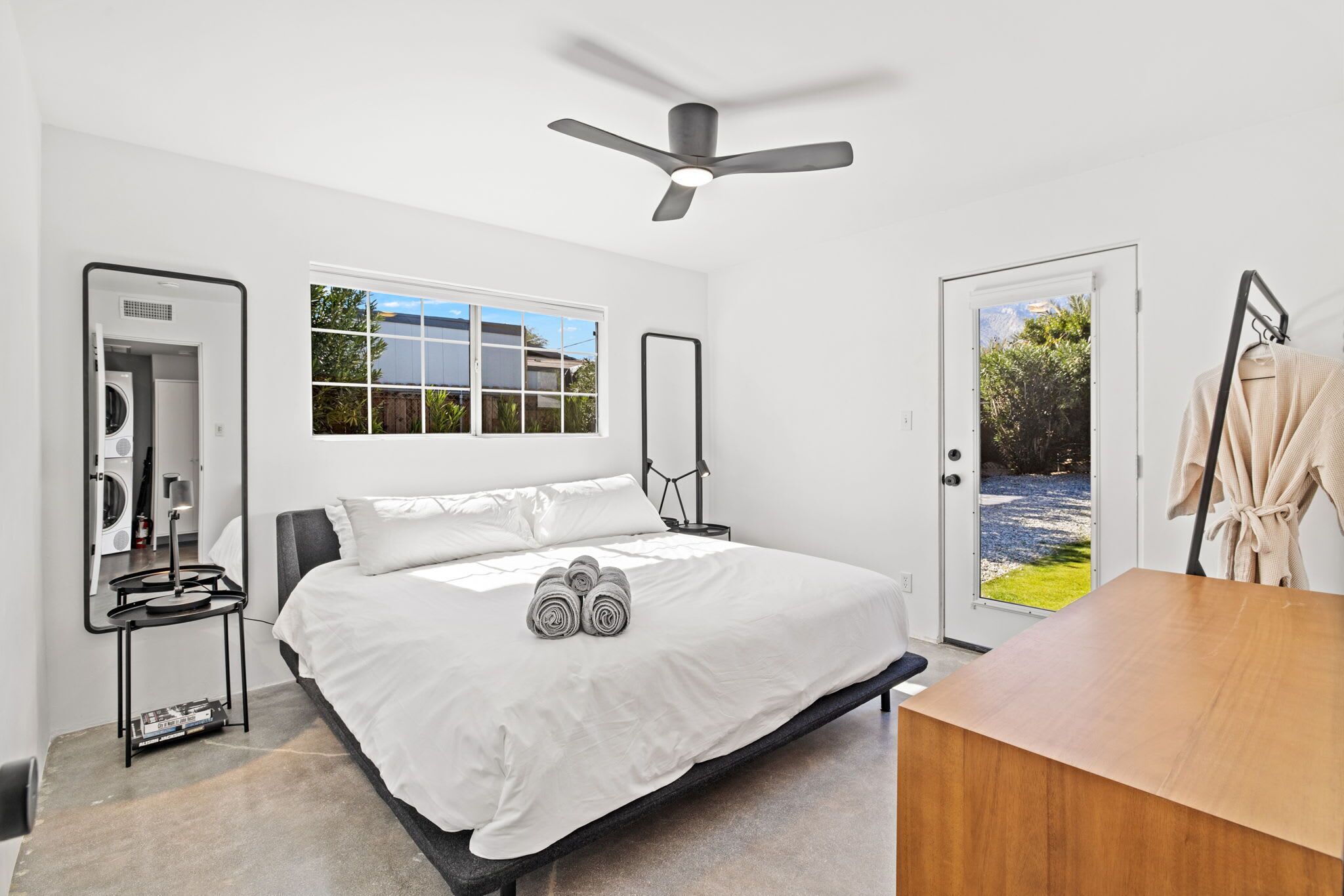Une chambre à coucher moderne avec un lit, un ventilateur de plafond, une fenêtre, une porte et une table en bois.