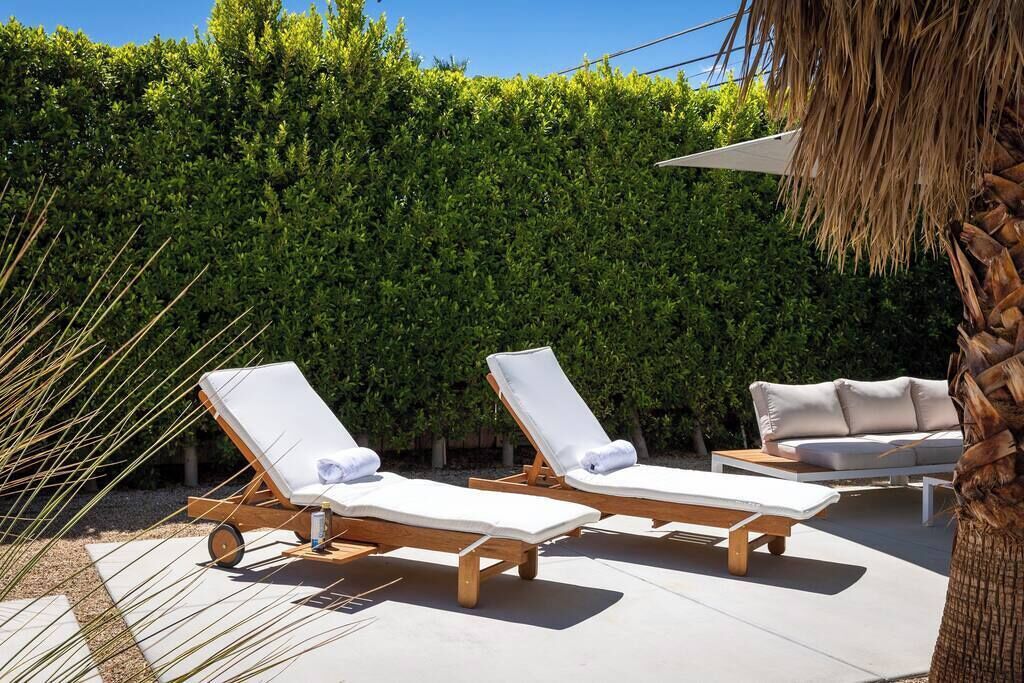 Un espace piscine comprenant deux chaises longues et un canapé, le tout entouré d’une haie.