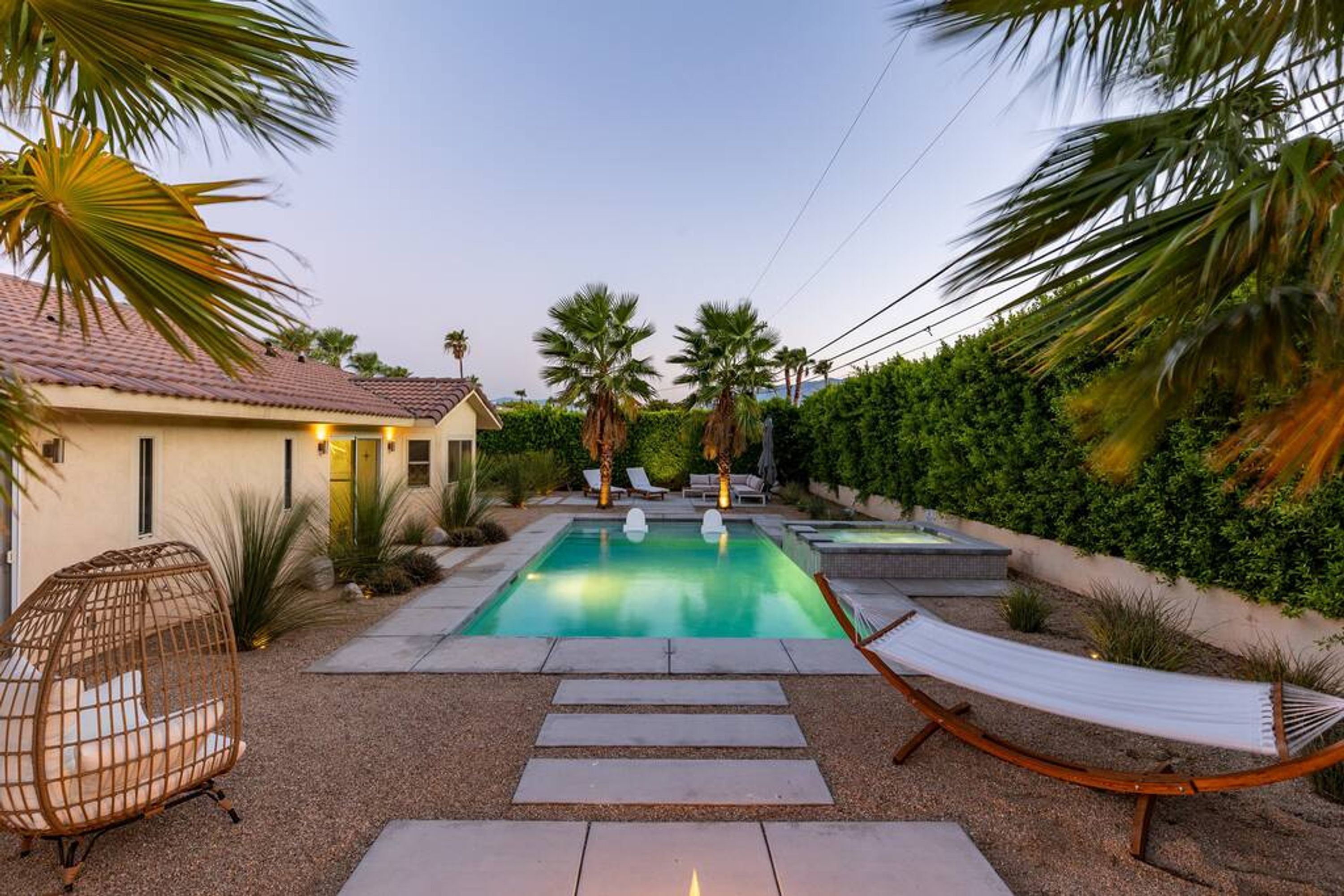 A swimming pool with a hammock, lounge chairs, and a house in the background.