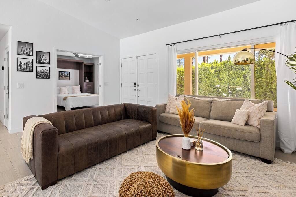 Una sala de estar moderna con un sofá de cuero marrón, un sofá beige y una mesa de centro redonda con un jarrón.