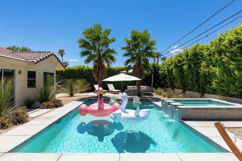 A swimming pool with two inflatable swans, surrounded by palm trees and a house.