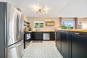 Uma cozinha moderna com frigorífico de aço inoxidável, armários pretos e chão de azulejos.