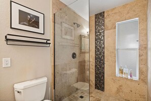 Casa de banho com cabine de duche em vidro, sanita, lavatório e espelho com artigos de higiene pessoal.
