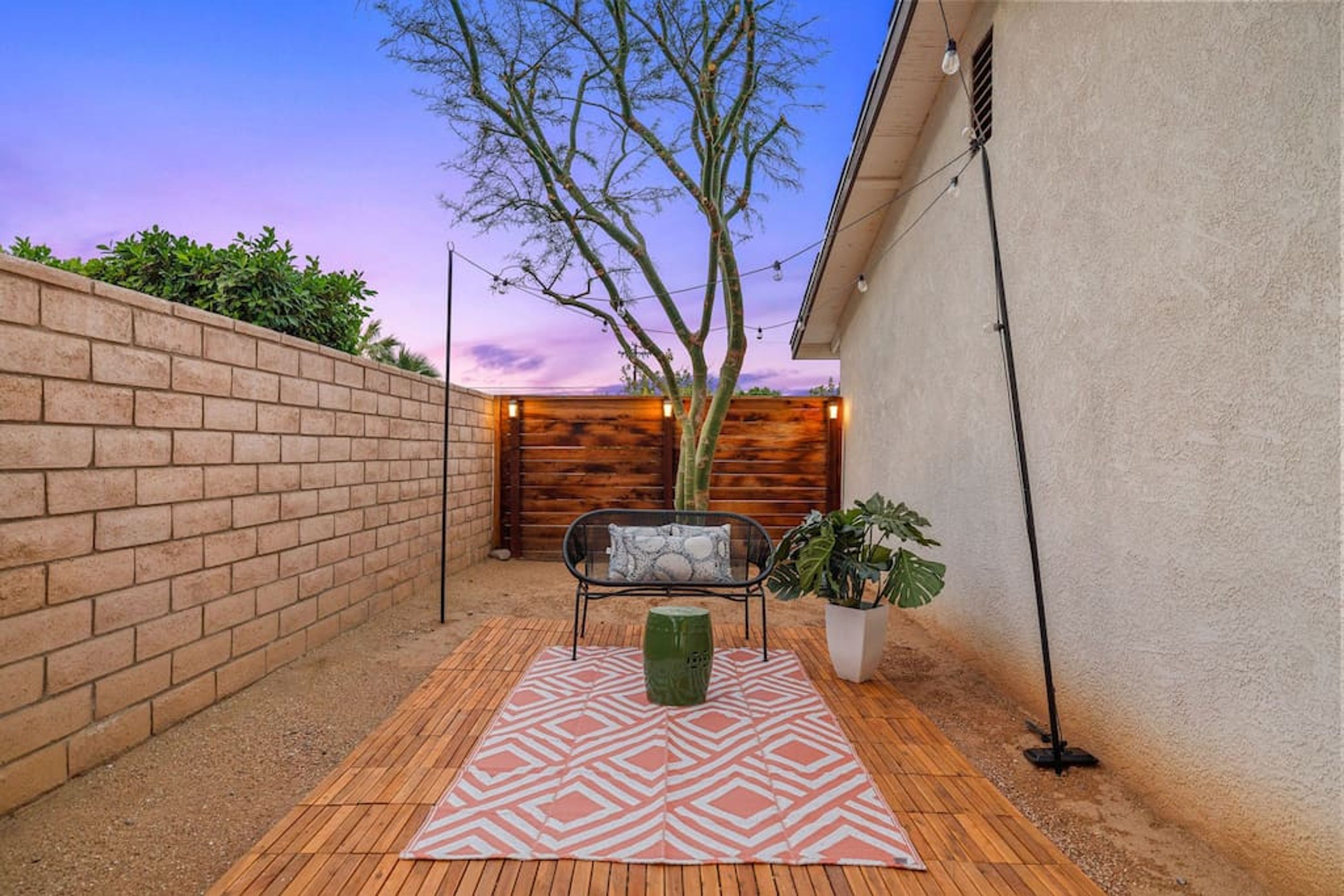 Un espace patio agrémenté d’un mur en briques, d’une clôture en bois, d’un banc, d’un pot de fleurs et d’un tapis à motifs.
