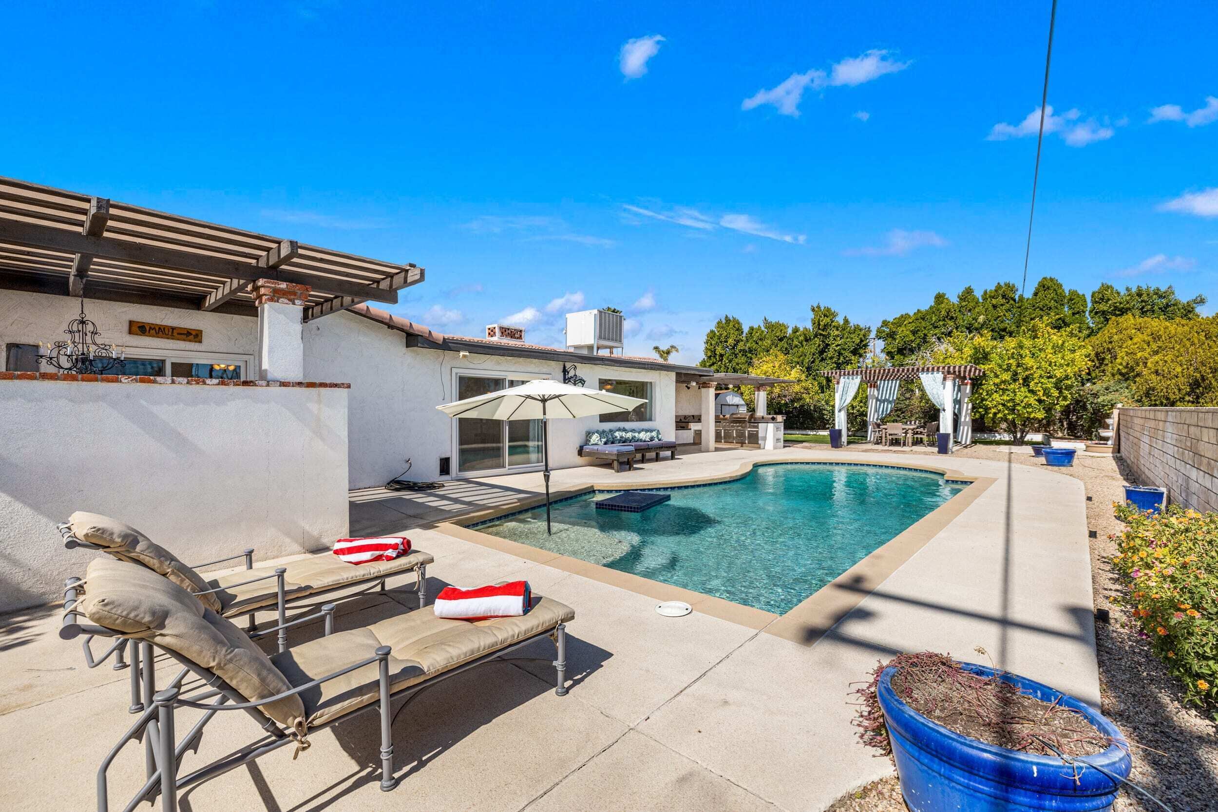 Un patio trasero con piscina, sillas de descanso y una pérgola.