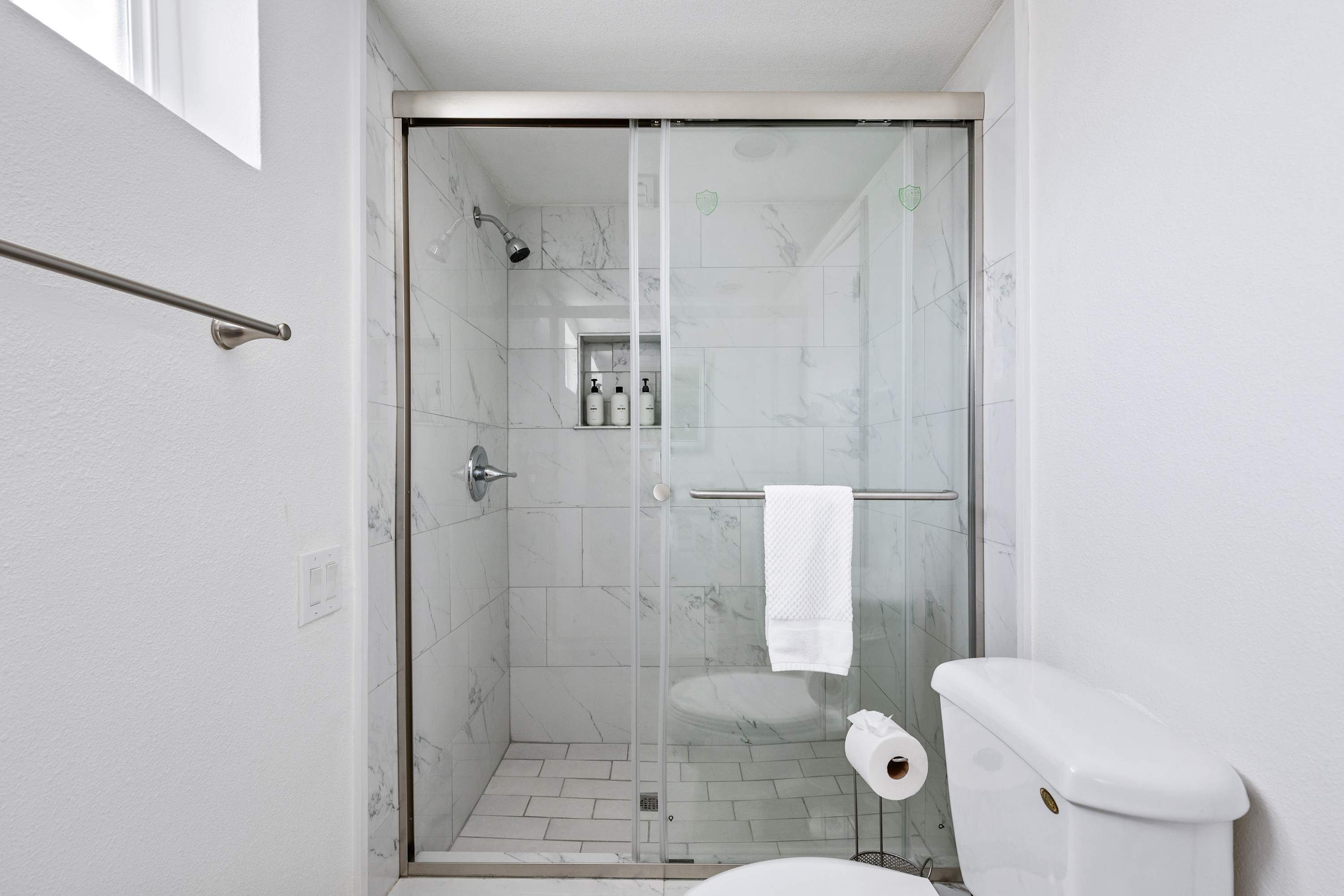 Une salle de bain moderne dotée d’une douche à parois de verre, de toilettes et d’un porte-serviettes.