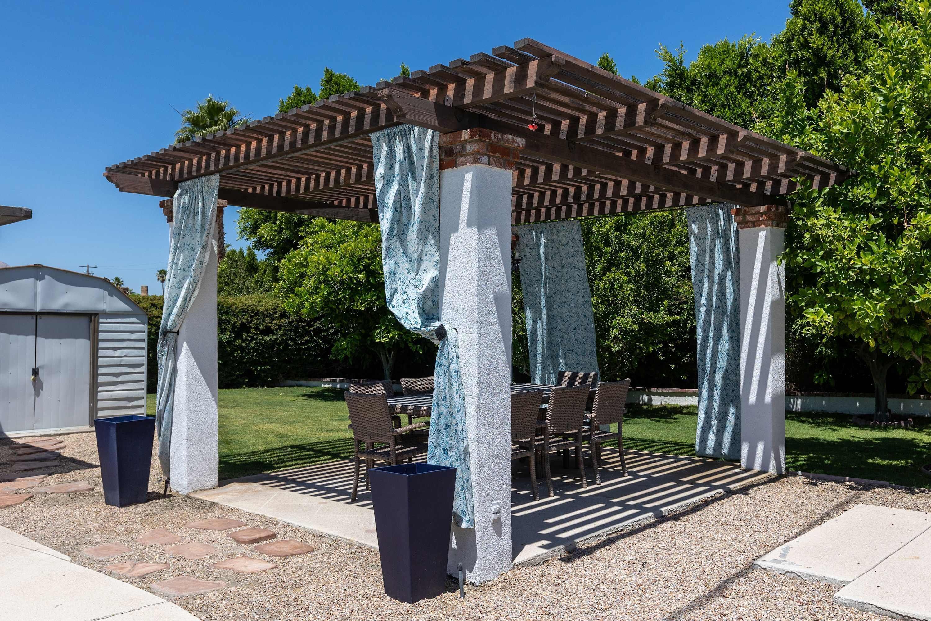 Ein überdachter Patio-Bereich mit Pergola, Sitzgelegenheiten im Freien und einem Mülleimer.