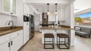 Une cuisine moderne avec des meubles blancs, des plans de travail en granit, des appareils électroménagers en acier inoxydable et un îlot central doté de tabourets.