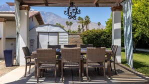 Une terrasse extérieure aménagée avec des meubles en osier, un lustre suspendu et une vue sur les montagnes en arrière-plan.