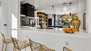 A modern kitchen with a white countertop, black and yellow striped wall, and a decorative golden vase with oranges. - The Escape Island (Palm Springs)