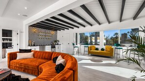 A modern living room with a curved orange sofa, a yellow sofa, and a dining area with green chairs. - The Escape Island (Palm Springs)