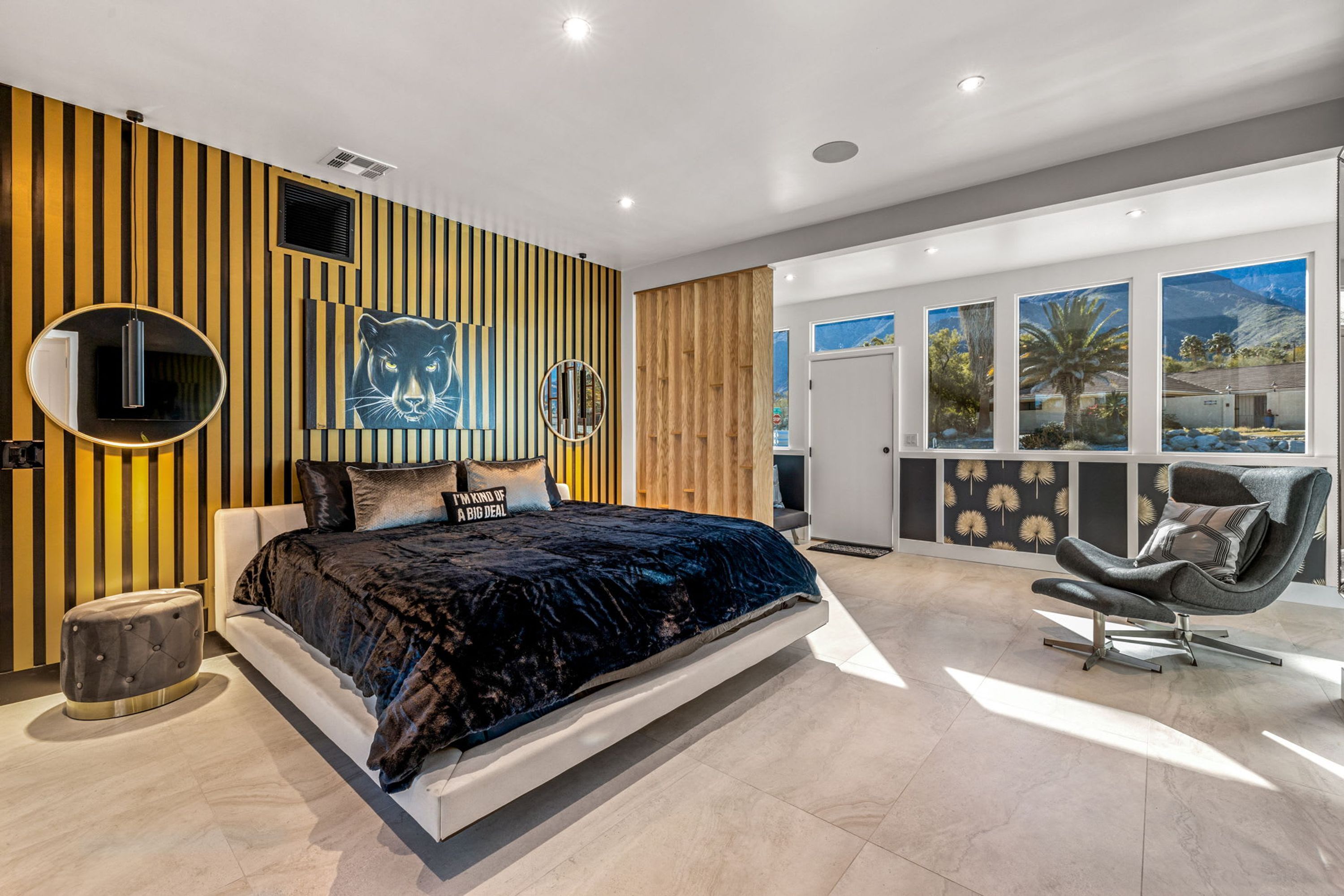 Une chambre moderne avec un grand lit, un miroir rond, une décoration murale sur le thème du tigre et une vue sur un paysage montagneux par la fenêtre.