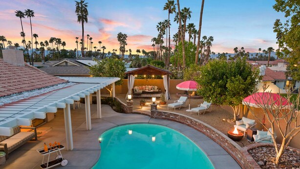 A swimming pool with a sunken seating area, surrounded by a brick wall and palm trees. - The Fig Ranch (Palm Springs)