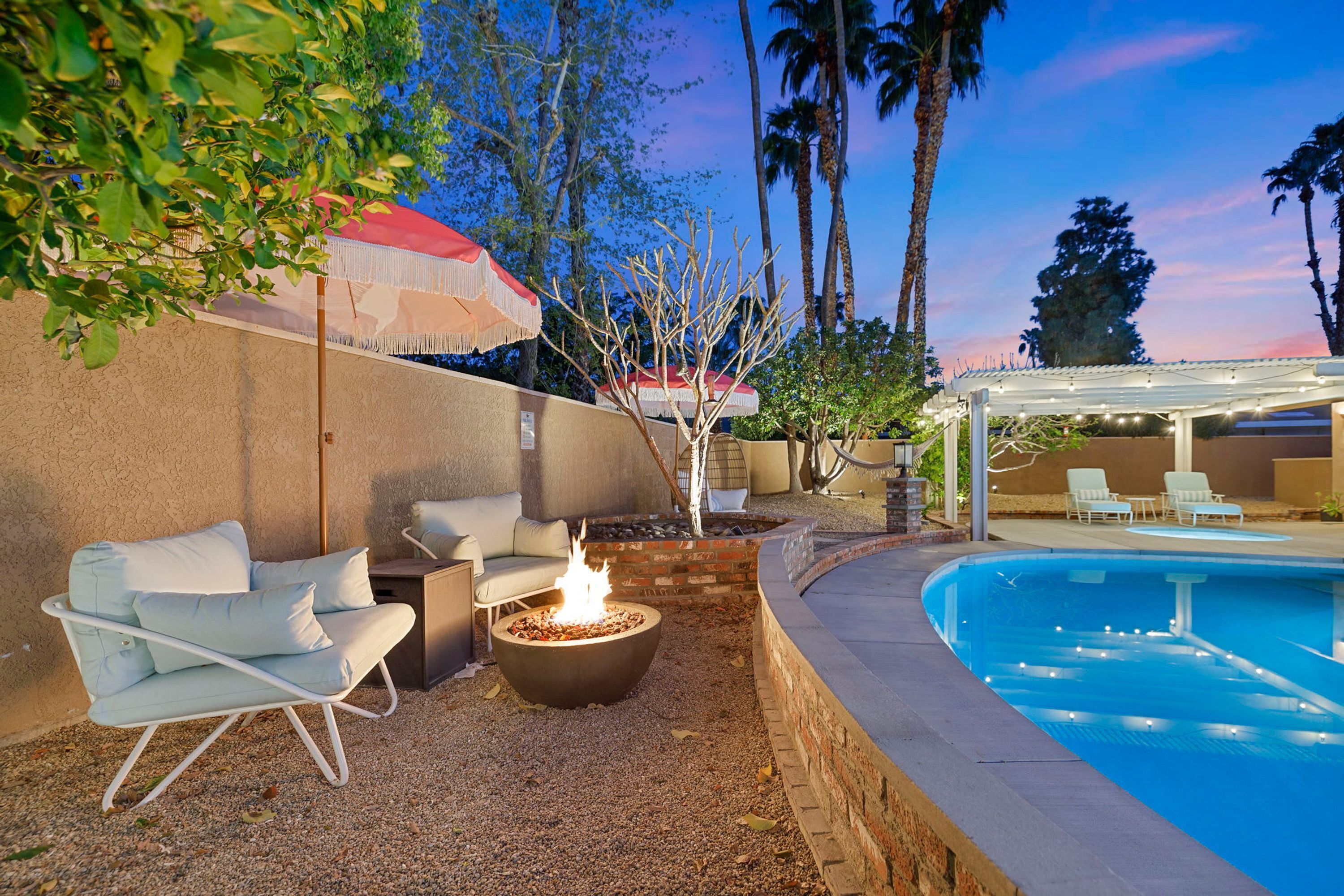 An outdoor pool area with a fire pit, lounge chairs, and a covered seating area.