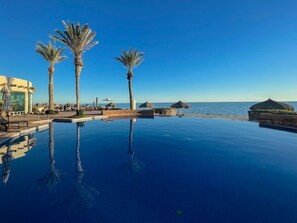 Ein klarer, blauer Himmel, ein ruhiger Pool, der Palmen widerspiegelt, und Blick auf das Meer.