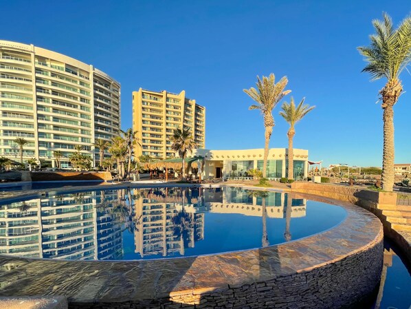 Et hotel med en stor swimmingpool, palmer og moderne arkitektur.