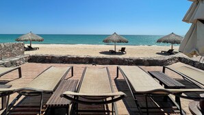 A beachside patio with lounge chairs and thatched umbrellas, overlooking the ocean. - Breathtaking Luxury Oceanfront Condo (Puerto Peñasco)