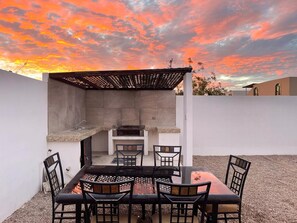 Una cocina al aire libre con una parrilla, zona de estar y una pérgola.