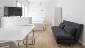 A modern, minimalist room with a white table, a grey sofa, a bed with white bedding, and a TV mounted on a white cabinet. - Al Mercato Delle Erbe by Wonderful Italy (Bologna)