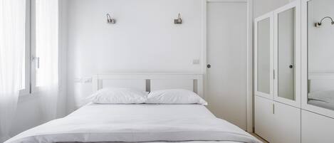 Minimalistinen makuuhuone, jossa on suuri sänky, lasiovilla varustettu vaatekaappi ja ovessa oleva kahva.