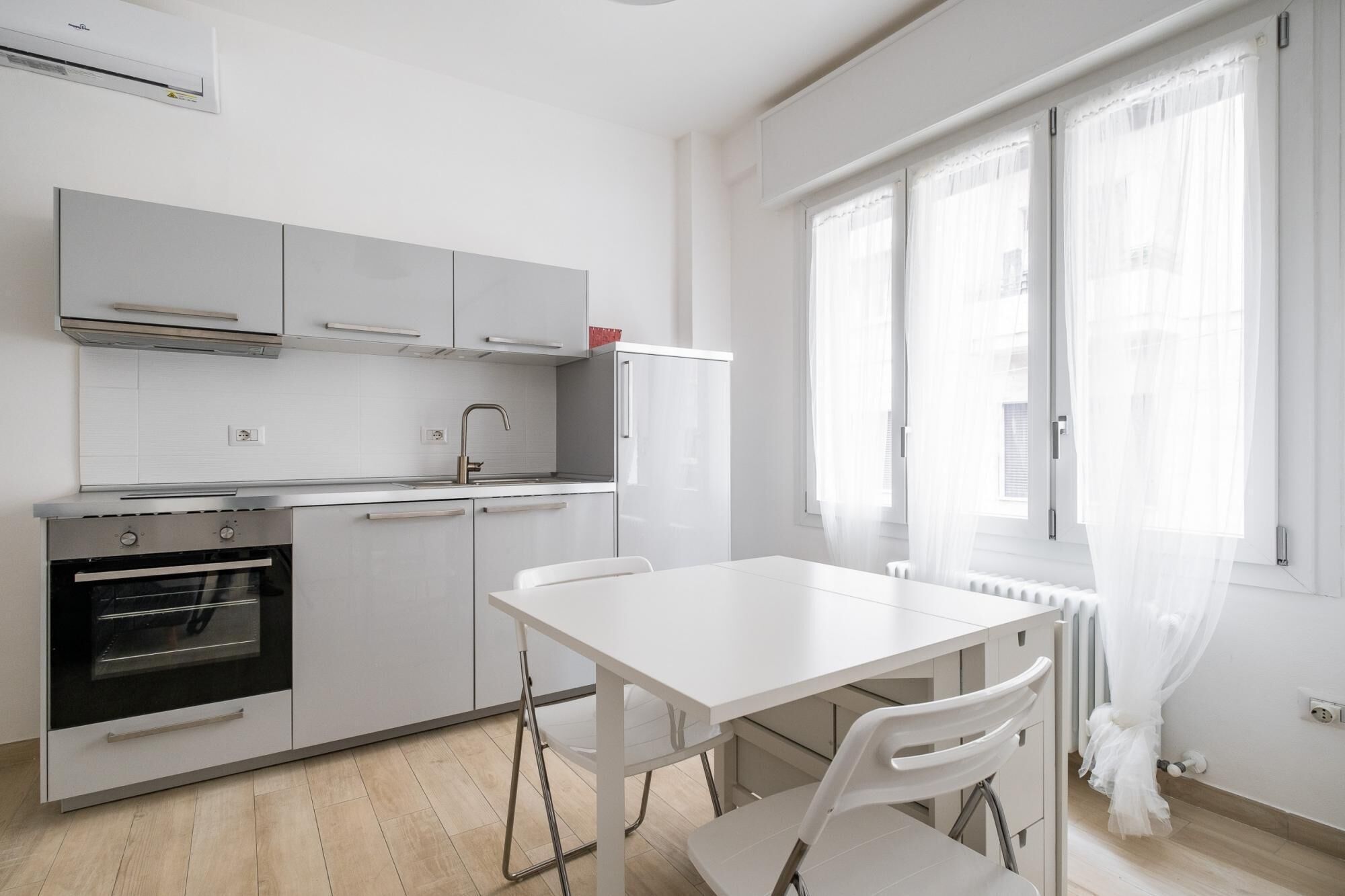 Une cuisine moderne avec des meubles blancs, un four encastré et une table à manger avec des chaises.