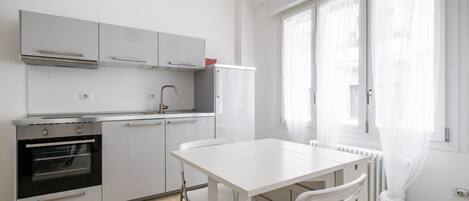Une cuisine moderne avec des meubles blancs, un four encastré et une table à manger avec des chaises.