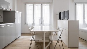 A modern kitchen with white cabinetry, a dining table with four chairs, and a flat-screen TV mounted above the counter. - Al Mercato Delle Erbe by Wonderful Italy (Bologna)