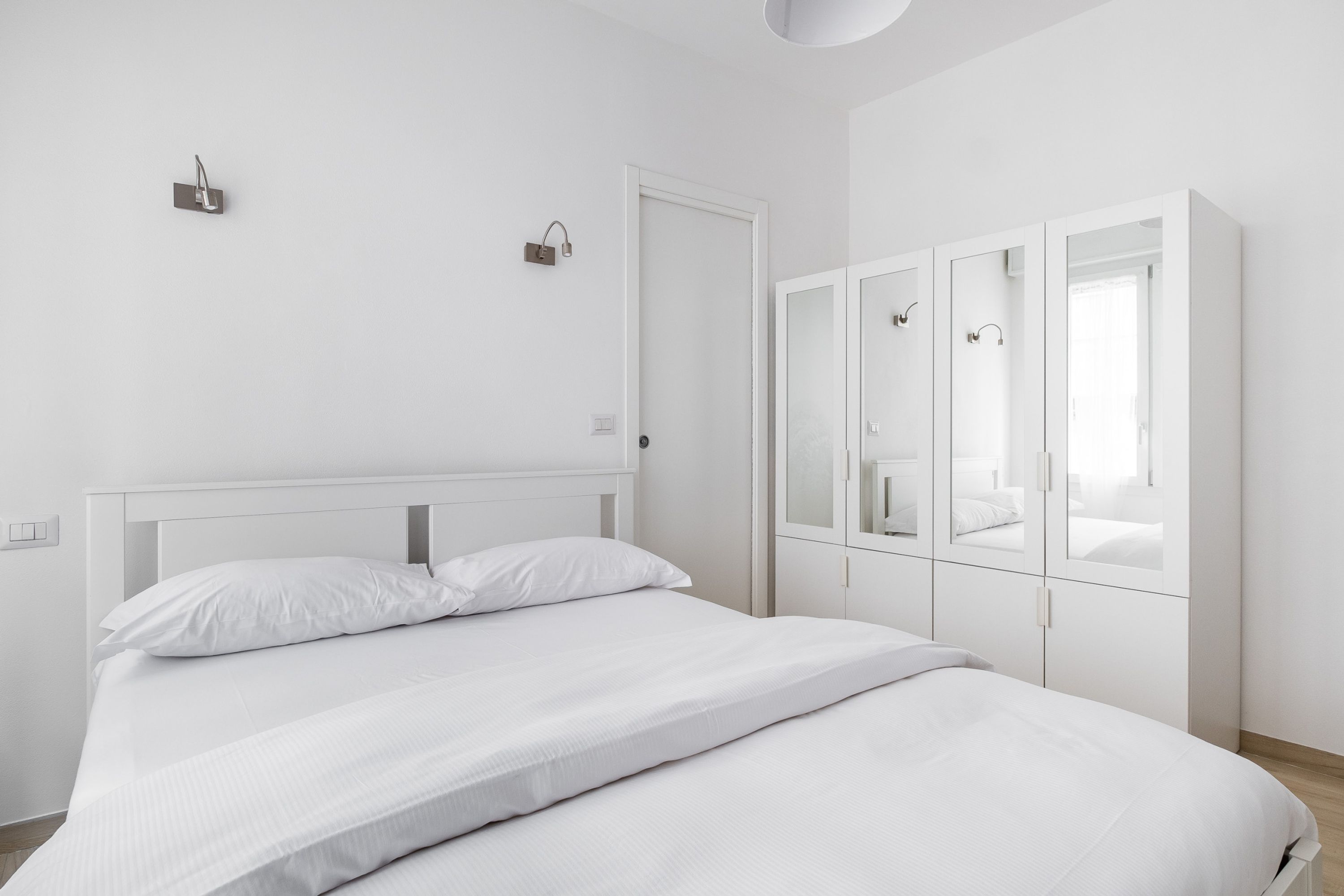 A minimalist bedroom with a bed, a wardrobe with mirrors, and a light fixture.
