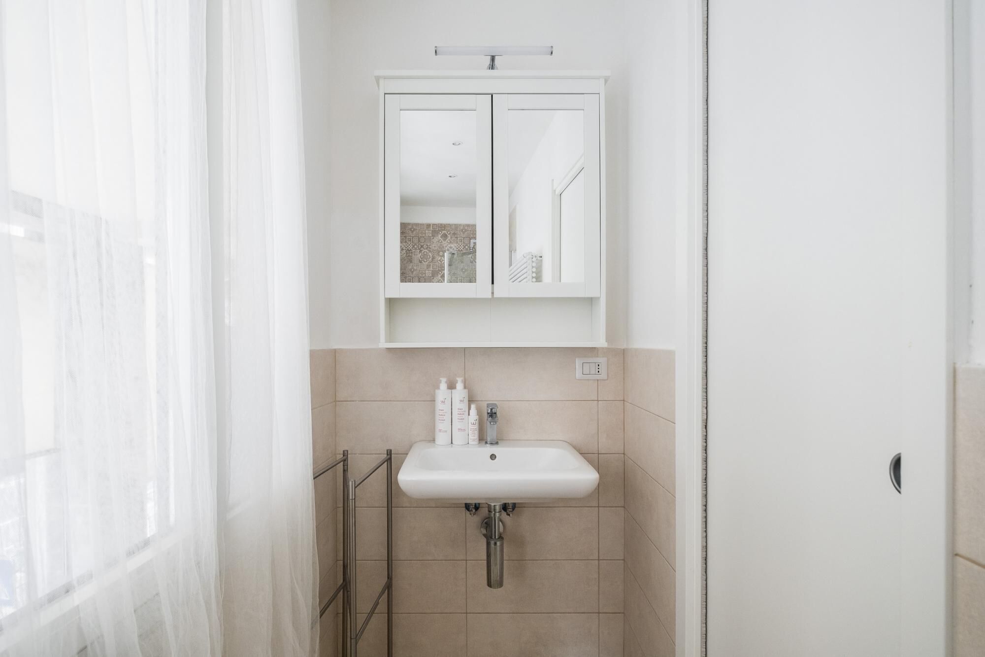 A bathroom with a white sink, a mirror above it, and a door to the right.