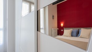 A bedroom with a bed, a red wall, a white radiator, and a nightstand with a lamp. - Graglia Modern Apartment by Wonderful Italy (Turin)