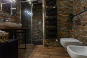 Ein modernes Badezimmer mit Steinwand, Duschkabine aus Glas, Waschbecken in Weiß und Toilette.
