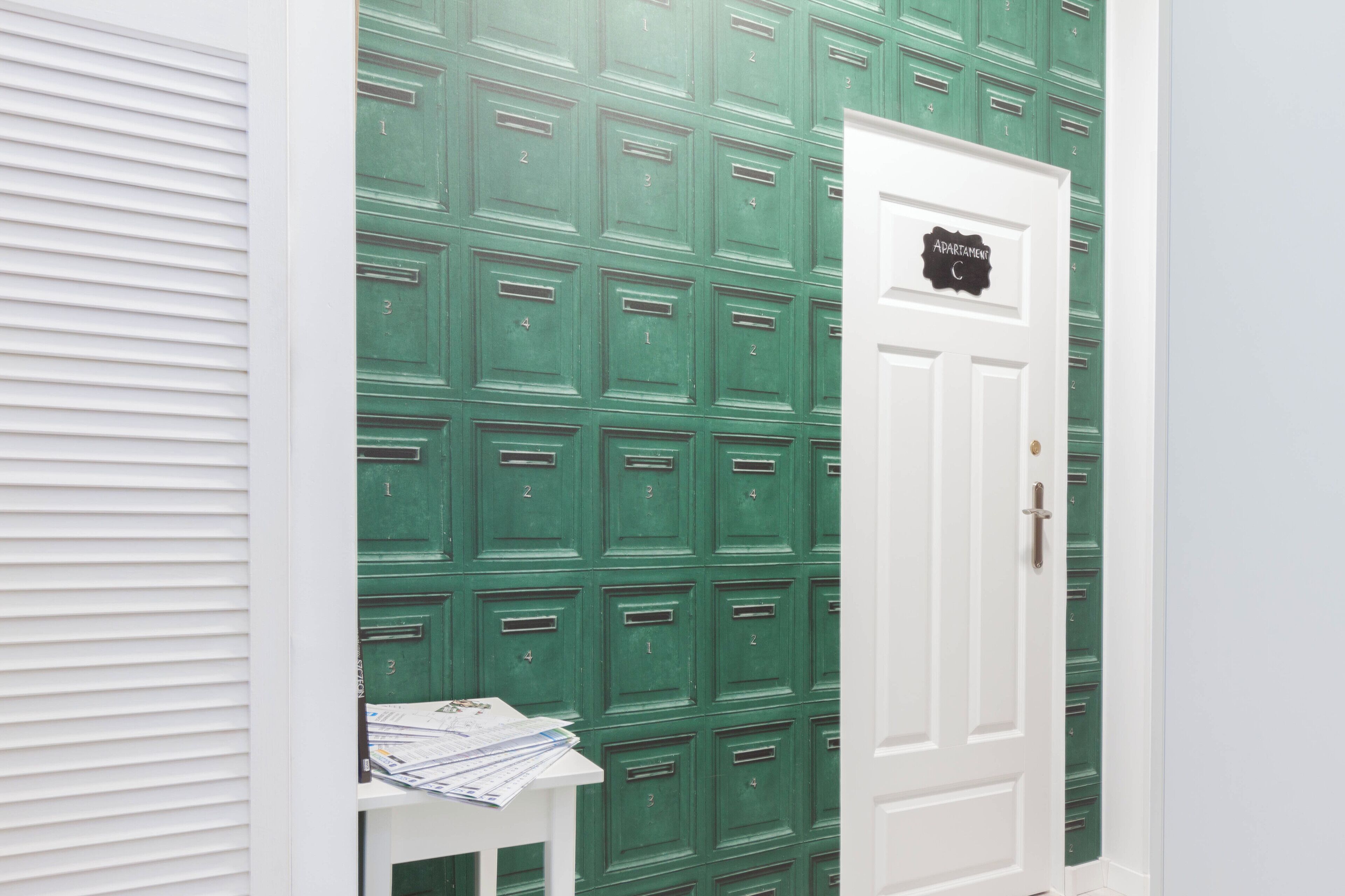 A room with a green locker wall, a white door labeled "Apartment C", and a small table with papers.