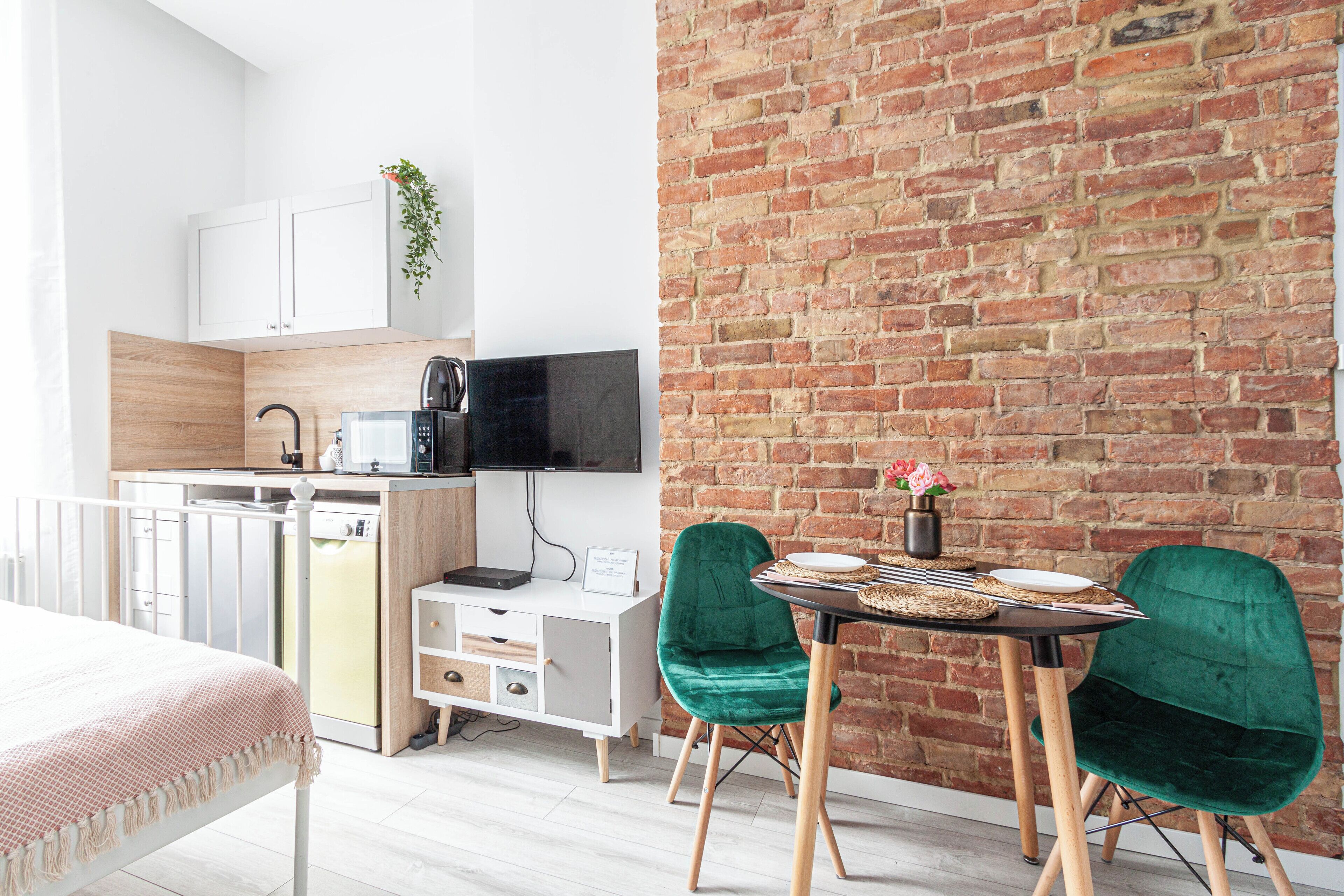 A modern kitchen with white cabinets, a microwave, and a coffee maker. There is a dining area with two green chairs and a small table.