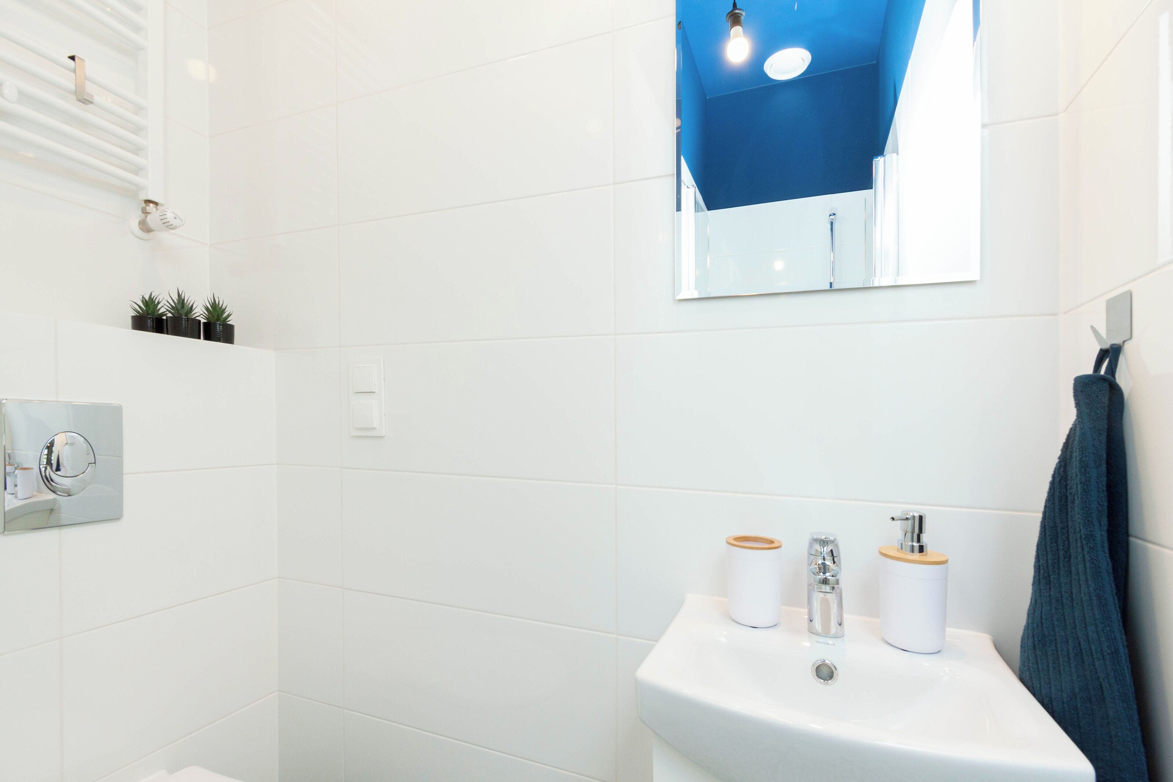 Een badkamer met witte tegels, een wastafel met twee doseerders, een spiegel en een handdoekrek.