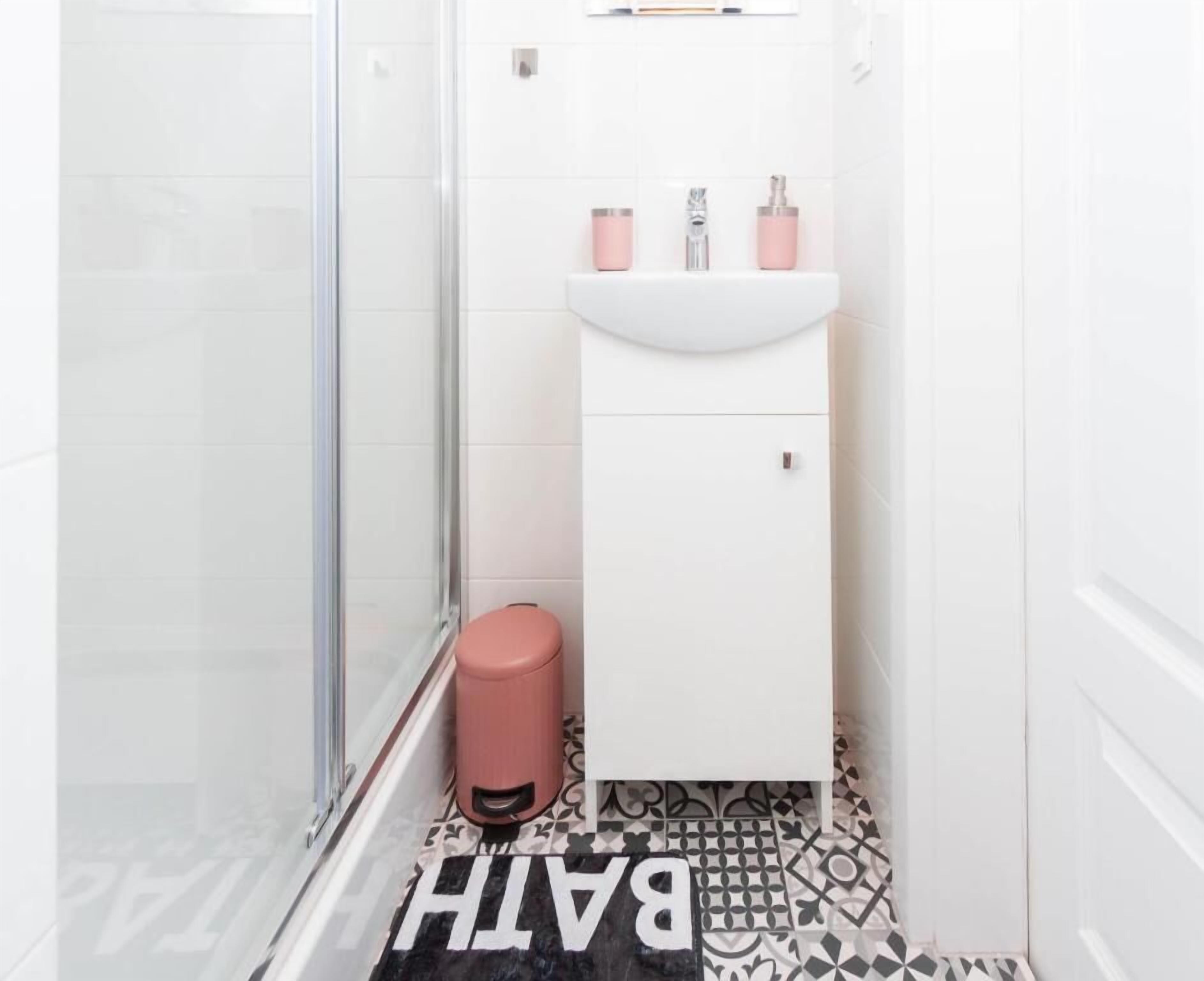 A bathroom with a glass shower enclosure, a white sink with pink accessories, and a patterned floor.