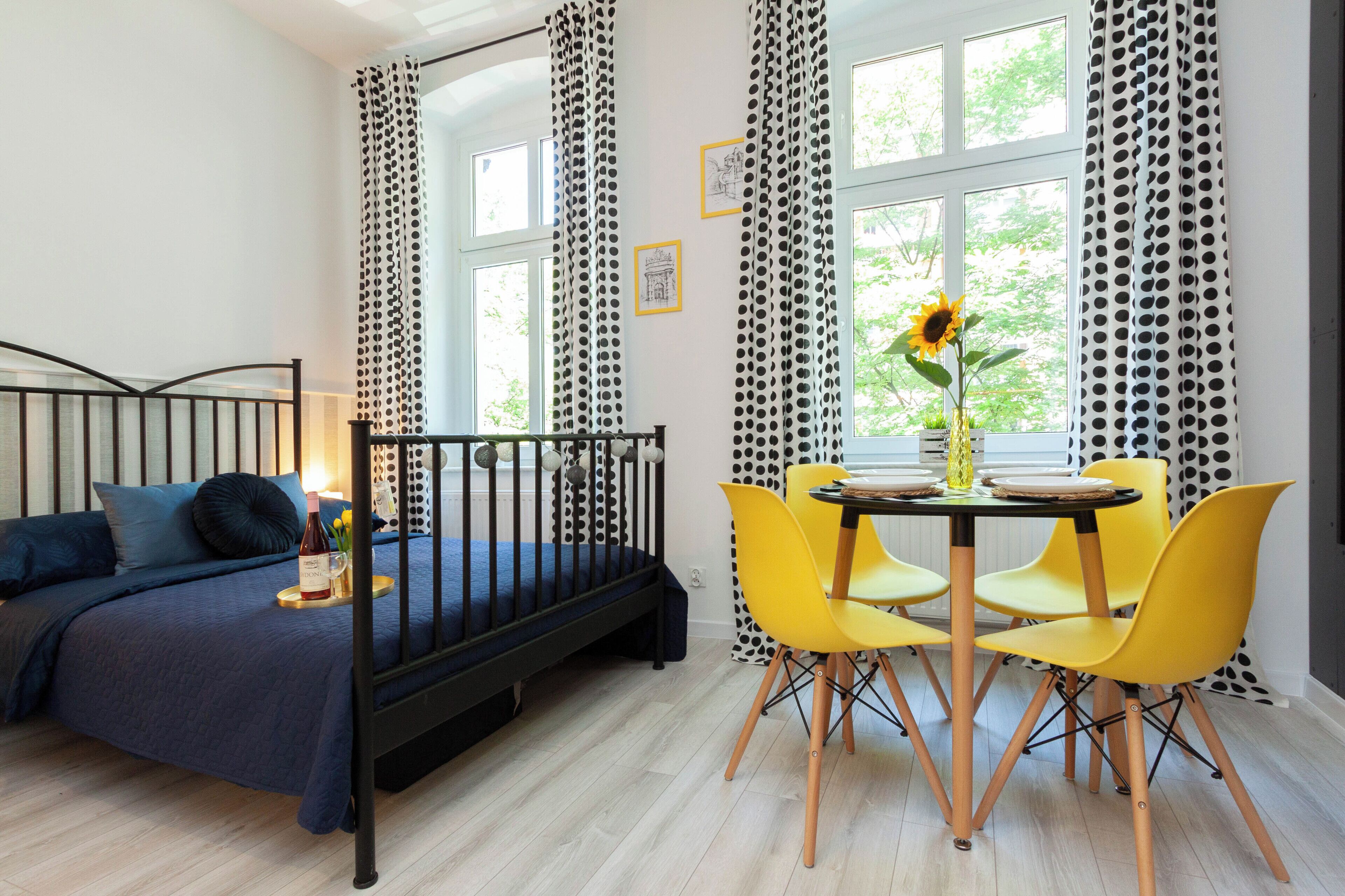 Un dormitorio con una cama, una mesa de comedor con sillas y una ventana con cortinas.