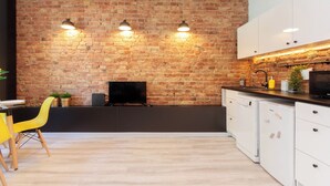 Una cocina con pared de ladrillo, armarios de madera, encimera negra y una silla amarilla.