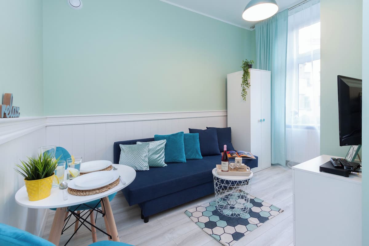Un salon moderne avec un canapé bleu, une petite table ronde ornée d’une plante et un meuble blanc.