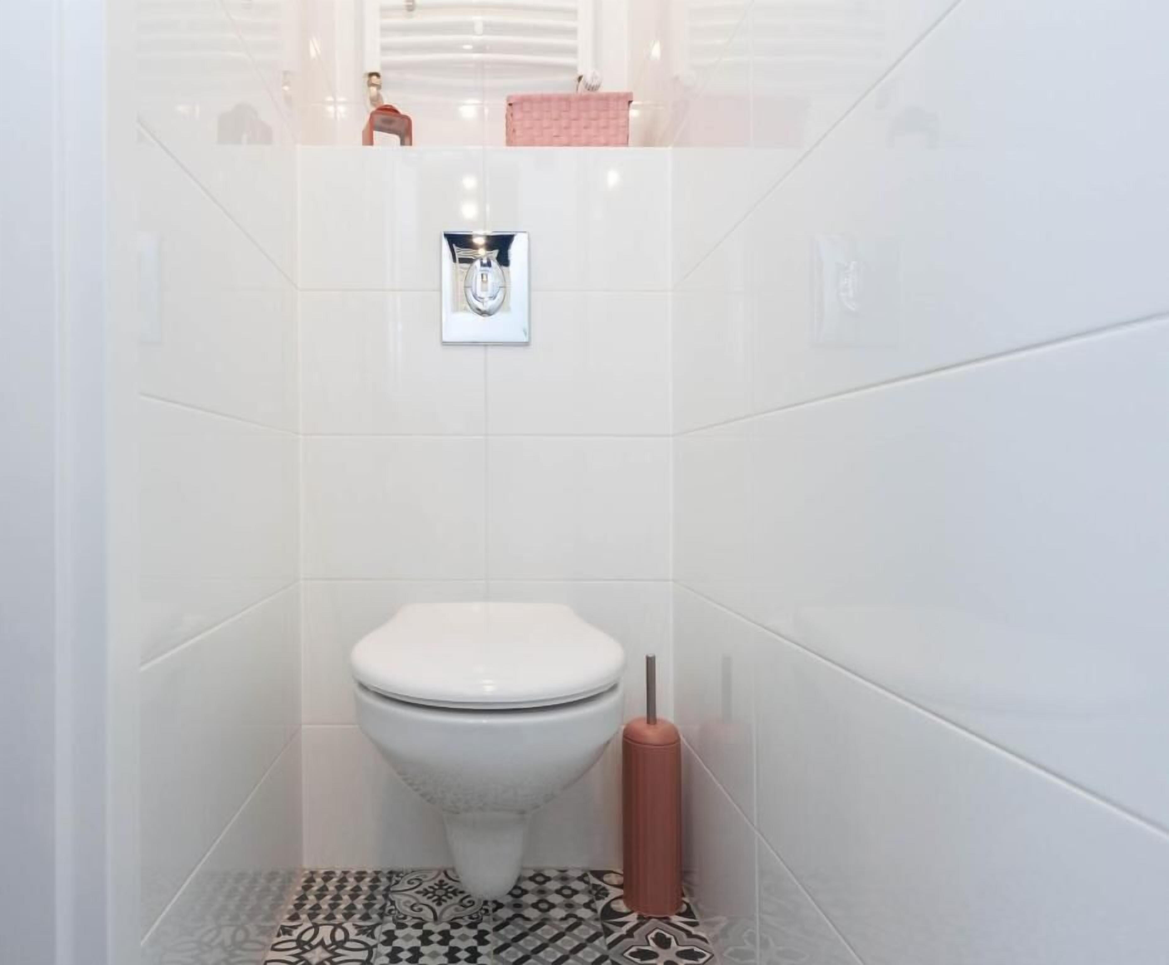 A small, white-tiled bathroom with a toilet, a hand dryer, and a towel rack.